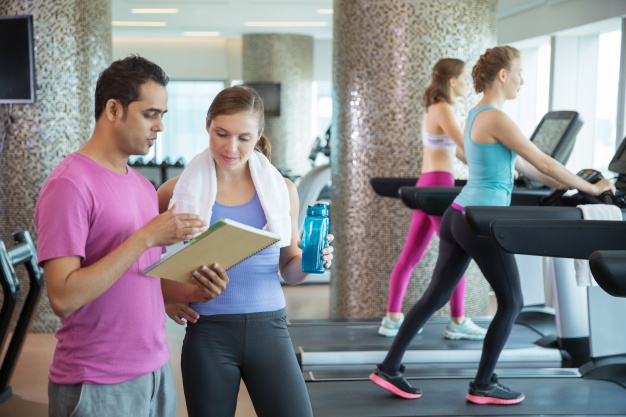 man and woman looking at a paper while two girls walk on the machines 1262 708